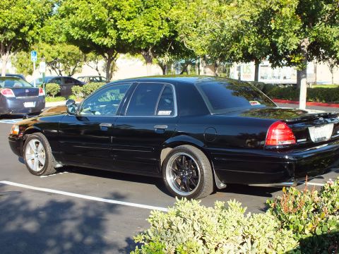2003 Ford Crown Victoria - Lowered black Crown Victoria parked in a striped space, full side view in sunlight.