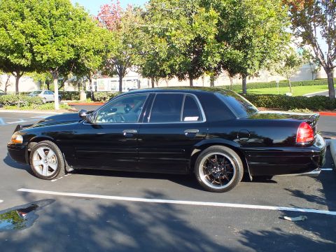 2003 Ford Crown Victoria - Lowered black Crown Victoria sedan parked beside hedges, full left profile.