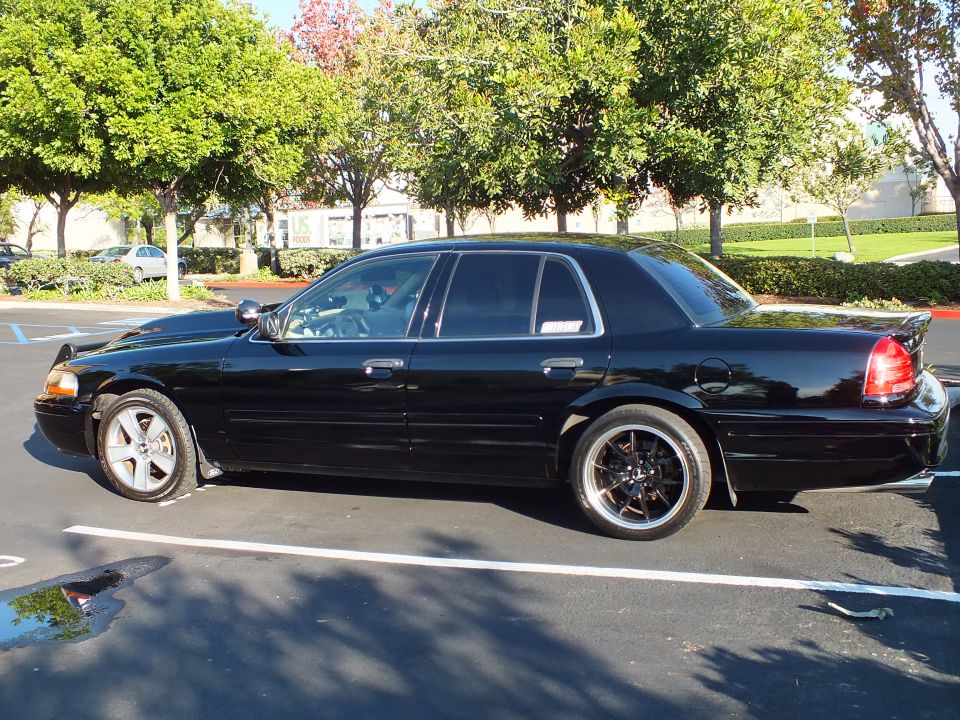 Black Ford Crown Victoria driver-side profile with silver front wheel and tinted glass