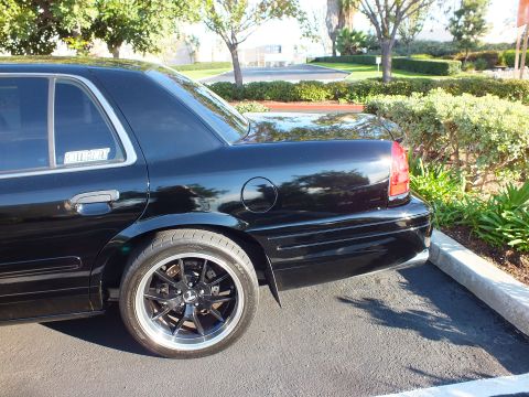 2003 Ford Crown Victoria - Detail shot of a black Crown Victoria rear quarter, fuel door and polished-lip wheel visible.