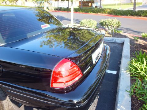 2003 Ford Crown Victoria - Tail light and decklid detail of a glossy black sedan parked next to landscaping.