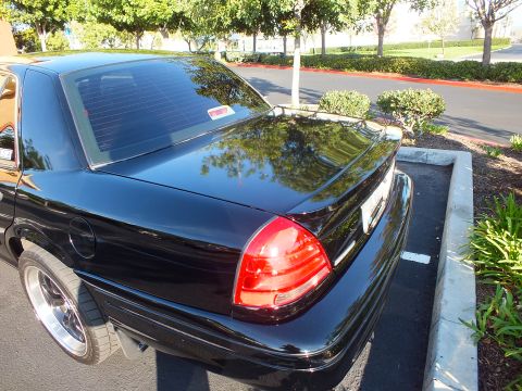 2003 Ford Crown Victoria - Glossy black sedan photographed from behind, trees mirrored in the deck lid and roof.
