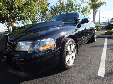 2003 Ford Crown Victoria - Front corner of a black sedan with clear headlight and amber marker, palms behind it.