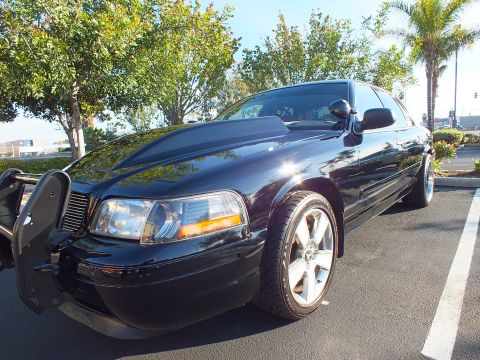 2003 Ford Crown Victoria - Lowered black sedan wearing a push bar, photographed from the front corner in a lot.