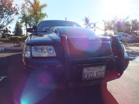 2003 Ford Crown Victoria - Front of a black sedan with grille guard and billet grille, lens flare across the frame.