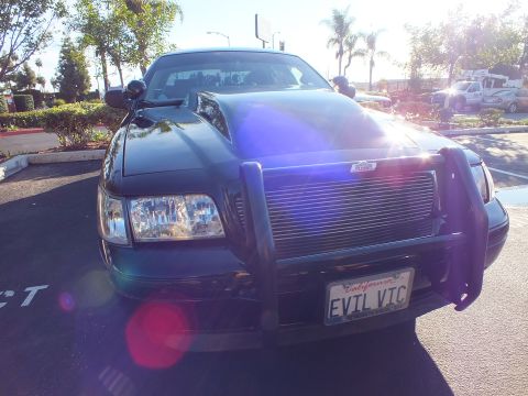 2003 Ford Crown Victoria - Front of a black sedan showing a pillar spotlight, push bar and billet grille in backlight.