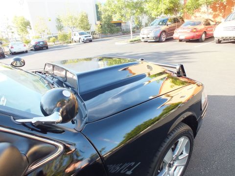 2003 Ford Crown Victoria - Hood, fender and chrome side mirror of a black sedan with parked cars beyond.