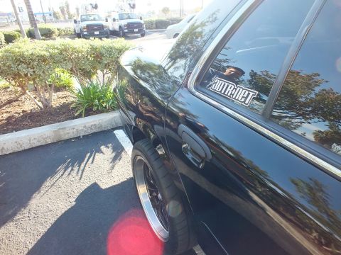 2003 Ford Crown Victoria - Rear quarter of a black sedan carrying an smtr.net window sticker, hedge alongside.