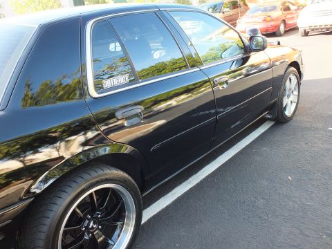 2003 Ford Crown Victoria - Rear door and wheel of a black sedan with a window decal and chrome mirror.