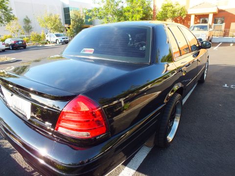 2003 Ford Crown Victoria - Right-rear view of a black sedan parked by landscaping, sky mirrored in the trunk.