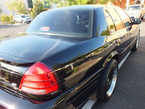 2003 Ford Crown Victoria - Passenger-rear view of a lowered black sedan, deep tint and polished wheels.