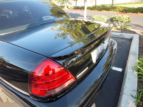 2003 Ford Crown Victoria - Deck lid and tail light of a black sedan, EVIL VIC plate visible, trees reflected.