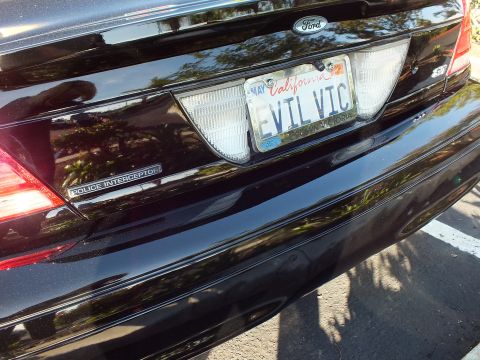 2003 Ford Crown Victoria - Close-up of a black Ford rear deck showing the EVIL VIC California plate above a Police Interceptor badge.