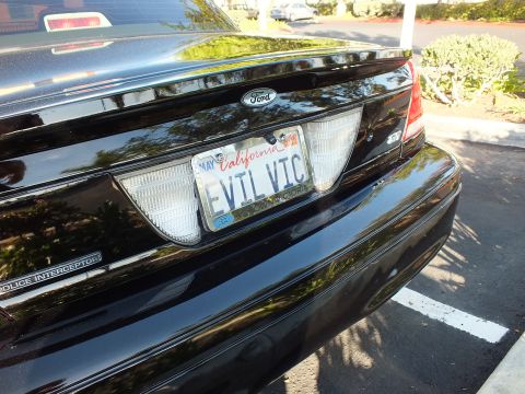 2003 Ford Crown Victoria - Rear deck of a black Ford sedan in a parking lot, EVIL VIC plate and Police Interceptor badge visible.