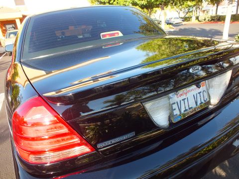 2003 Ford Crown Victoria - Black Ford sedan rear quarter showing the red taillight, EVIL VIC plate and Police Interceptor trunk lettering.