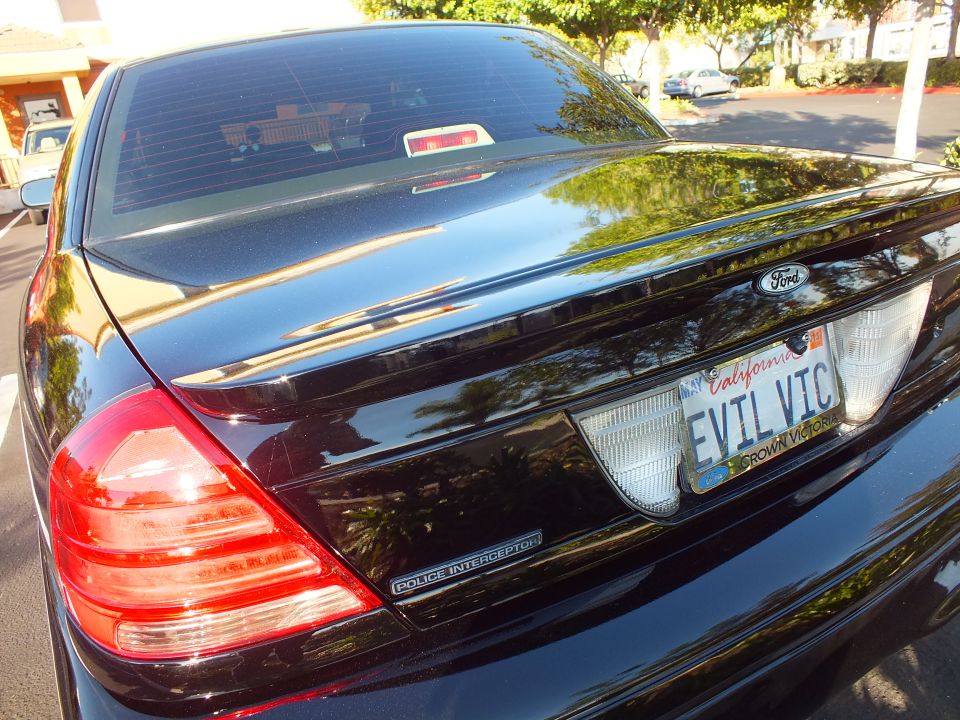 Rear three-quarter of black Ford Crown Victoria with EVIL VIC plate, taillight and Police Interceptor badge