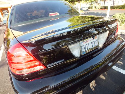 2003 Ford Crown Victoria - Black Ford decklid and taillight catch low sun, EVIL VIC plate and Police Interceptor badge in view.