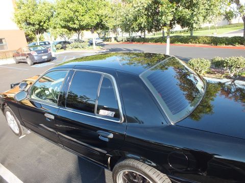 2003 Ford Crown Victoria - Elevated side-rear view of a black Ford sedan showing tinted quarter glass and a white window decal.