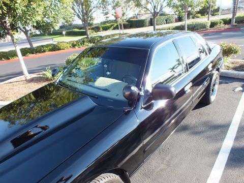 2003 Ford Crown Victoria - Low front-quarter shot of a black Ford sedan in a lot, reflective hood and tinted windshield.