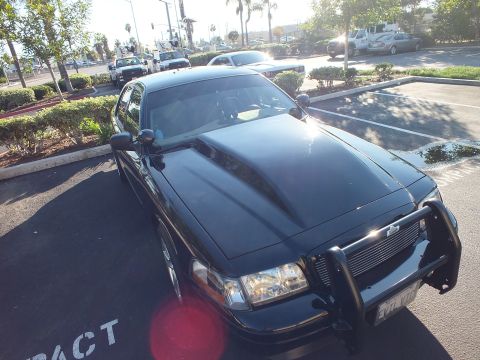 2003 Ford Crown Victoria - Elevated front-quarter view of a black Ford with push bar and billet grille, lens flare on hood.