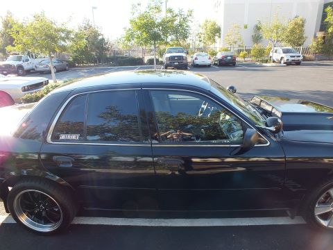 2003 Ford Crown Victoria - Side profile of a black Ford sedan, lowered stance on black wheels and a white quarter-glass decal.