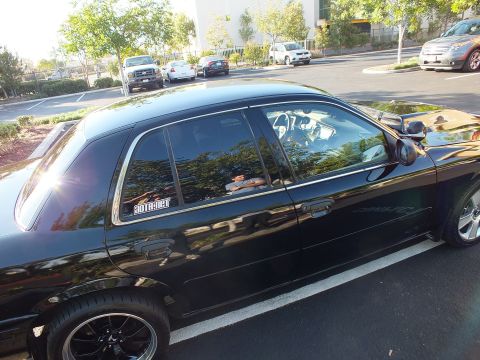 2003 Ford Crown Victoria - Glossy black Ford sedan side view showing chrome trim, black wheels and a white window decal.
