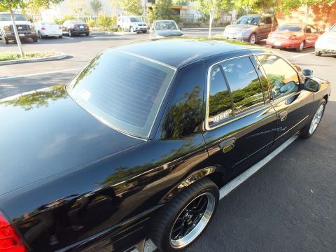 2003 Ford Crown Victoria - Elevated rear-quarter view of a black Ford sedan with dark tint and black wheels among parked cars.