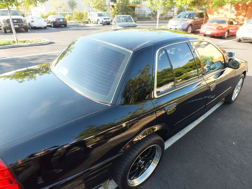 Rear three-quarter of black Ford Crown Victoria with tinted glass and black wheels in parking lot