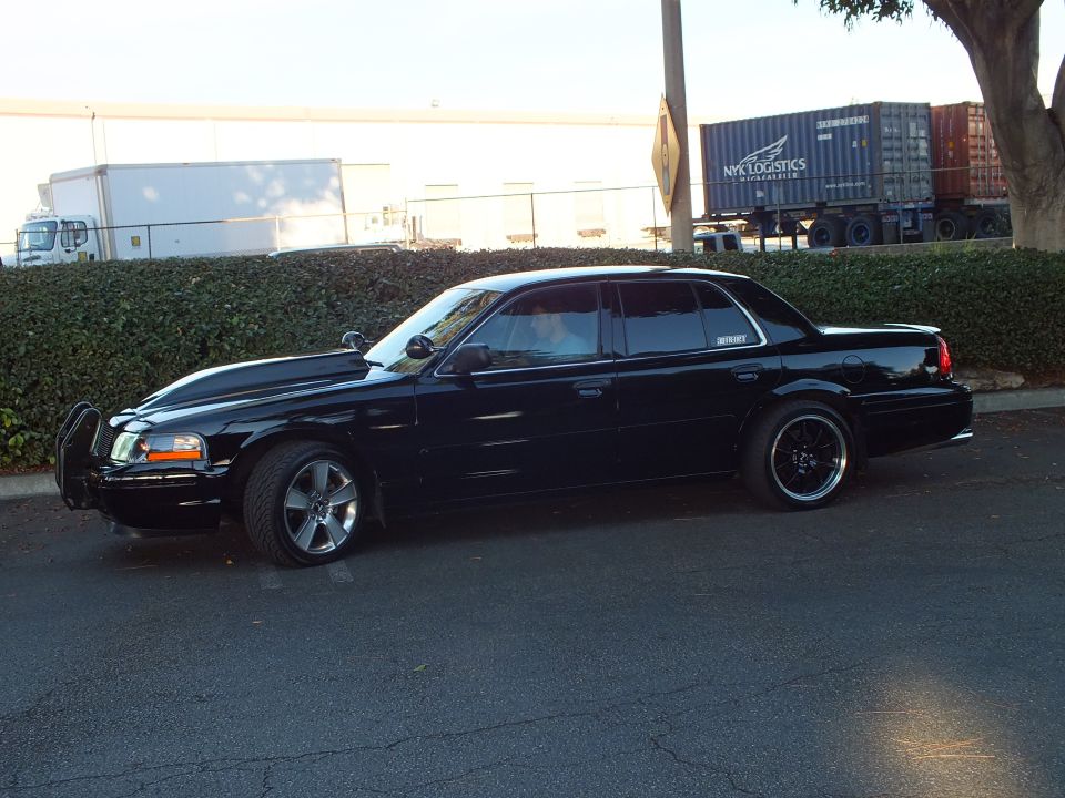 Side profile of lowered black Ford Crown Victoria with brush guard and black wheels by shipping containers