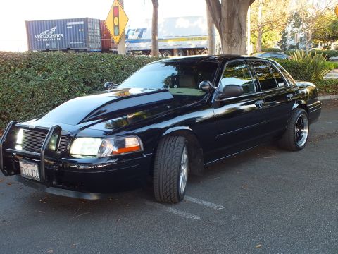 2003 Ford Crown Victoria - Side-front of a lowered black Crown Vic with staggered black wheels, shipping containers in the background.