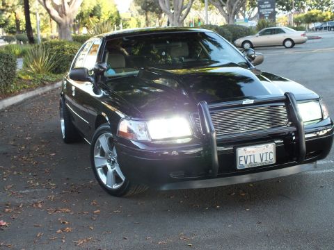 2003 Ford Crown Victoria - Dark Crown Vic angled in a lot, billet grille behind a chrome guard, plate reads EVIL VIC.
