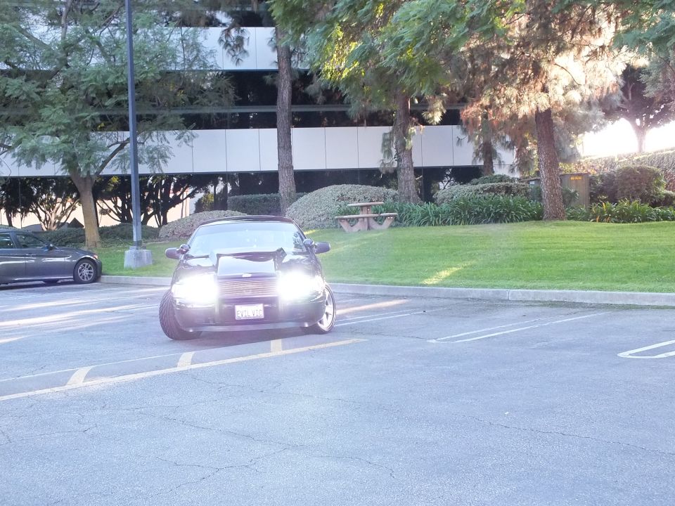 Dark sedan parked in office lot at distance, headlights on, building behind