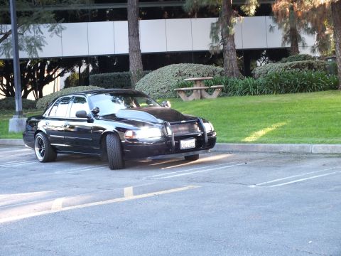 2003 Ford Crown Victoria - Black Crown Vic parked in an office lot with a chrome push bar, lawn and picnic table behind.