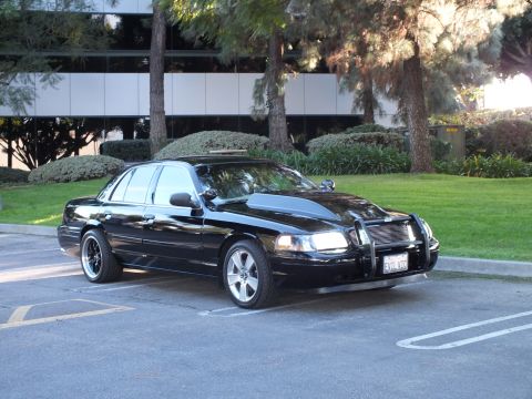 2003 Ford Crown Victoria - Black Crown Vic angled in an office lot, billet grille and chrome guard, machined wheels, lawn behind.