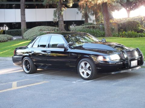 2003 Ford Crown Victoria - Side-front profile of a black Crown Vic on machined wheels, chrome guard up front, office lot setting.