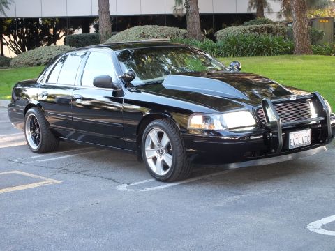 2003 Ford Crown Victoria - Glossy black Crown Vic on machined wheels with a chrome push bar, plate reads EVIL VIC, lawn behind.
