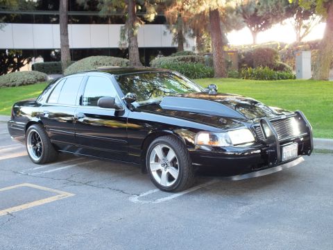2003 Ford Crown Victoria - Front-quarter shot of a blacked-out Crown Victoria with push bar, A-pillar spotlight, and chrome wheels.