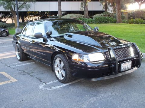 2003 Ford Crown Victoria - Crown Victoria front quarter view showing brush guard, billet grille, spotlight, against an office facade.