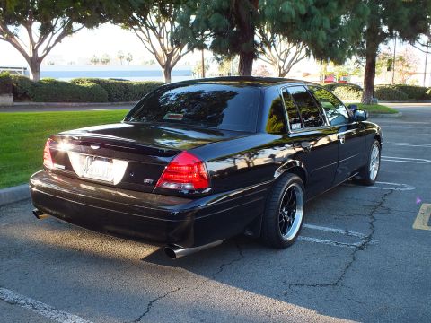 2003 Ford Crown Victoria - Black Crown Victoria from rear quarter, GT trunk badge, dark wheels and turned-down exhaust, parking lot.