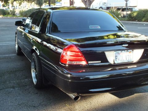 2003 Ford Crown Victoria - Low-angle rear quarter of black Crown Victoria, deep chrome-lip wheels, EVIL VIC plate, single visible tip.