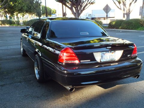 2003 Ford Crown Victoria - Black Crown Victoria rear-three-quarter, lit taillight and chrome exhaust tip, street parking near a sign.