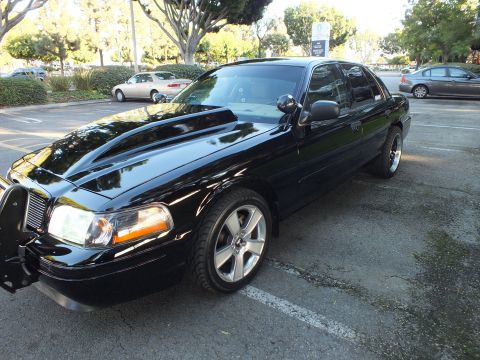2003 Ford Crown Victoria - High-angle front quarter of black Crown Victoria showing raised cowl hood, billet grille and brush guard.