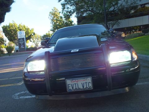 2003 Ford Crown Victoria - Head-on view of black Crown Victoria with brush guard, billet grille, lit headlights, EVIL VIC plate.