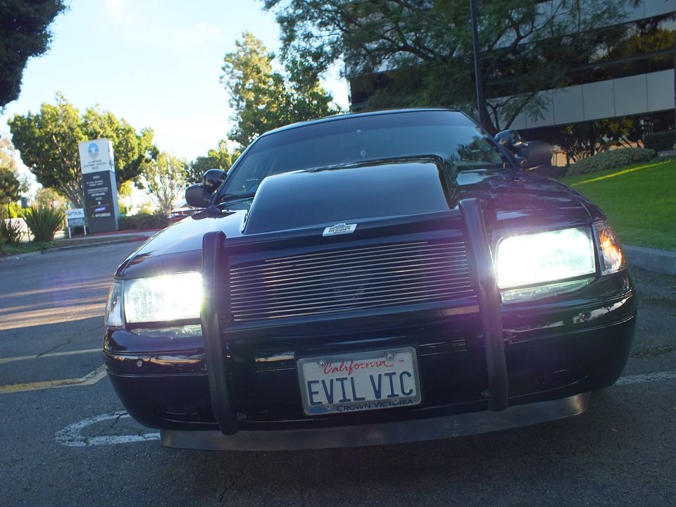 Front of black Ford Crown Victoria, headlights on, billet grille, EVIL VIC California plate