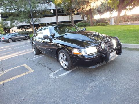 2003 Ford Crown Victoria - Black Crown Victoria front-three-quarter, brush guard and billet grille, amber side markers, parking lot.