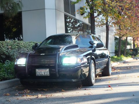 2003 Ford Crown Victoria - Head-on dusk shot of dark Crown Victoria, lit headlights, brush guard, billet grille, EVIL VIC plate.