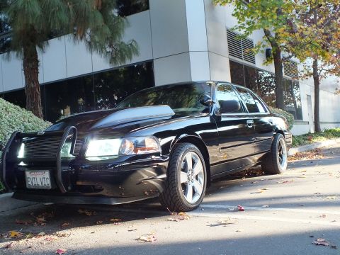 2003 Ford Crown Victoria - Front-quarter view of black Crown Victoria with brush guard and billet grille, leaves on the ground.