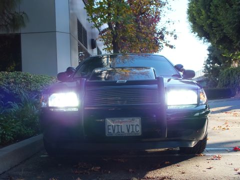 2003 Ford Crown Victoria - Head-on shot of a blacked-out Crown Victoria sedan, headlights lit, push-bar guard framing a billet grille marked EVIL VIC.