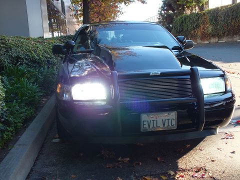 2003 Ford Crown Victoria - Curbside three-quarter view of a black full-size sedan, push bar and chrome billet grille over an EVIL VIC plate.