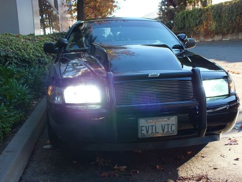 2003 Ford Crown Victoria - Low-angle front-quarter of a black sedan with grille guard, lit headlights and an EVIL VIC vanity plate.
